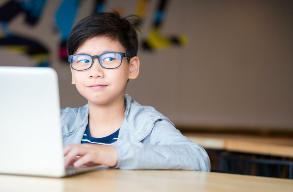 A child with blue light reflected on his glasses from a laptop