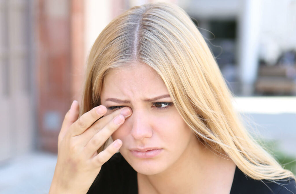 Close-up of a woman with blonde hair rubbing her right eye with her right hand.