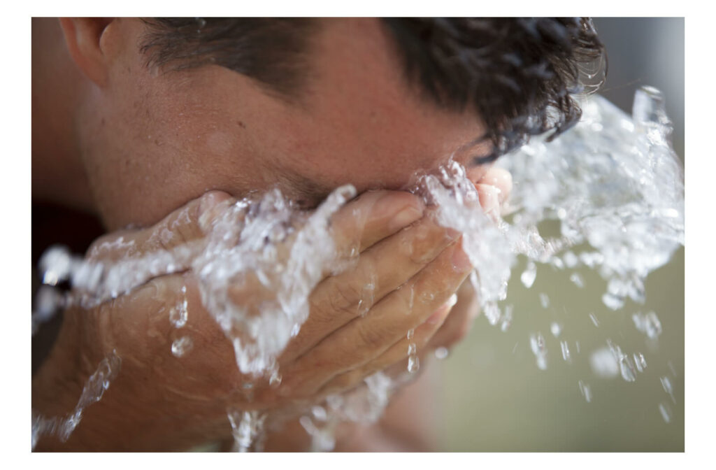 A man splashes his face with water to remove an eyelash stuck in his eye