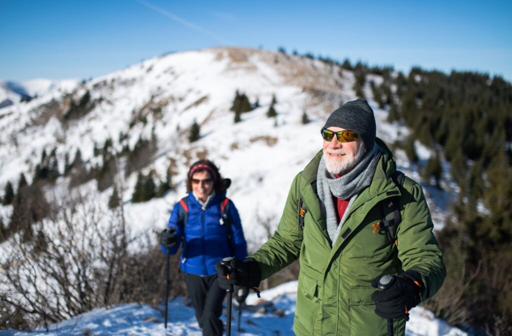 A senior couple each wearing sunglasses as they enjoy a winter hike together.