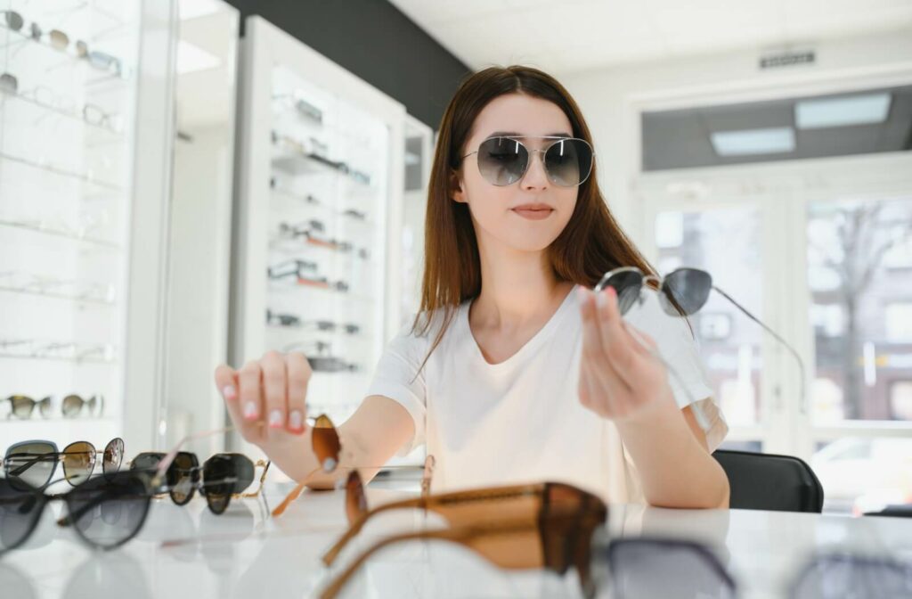 A woman wearing large aviator sunglasses while browsing and selecting from a variety of frames at an eyewear boutique.